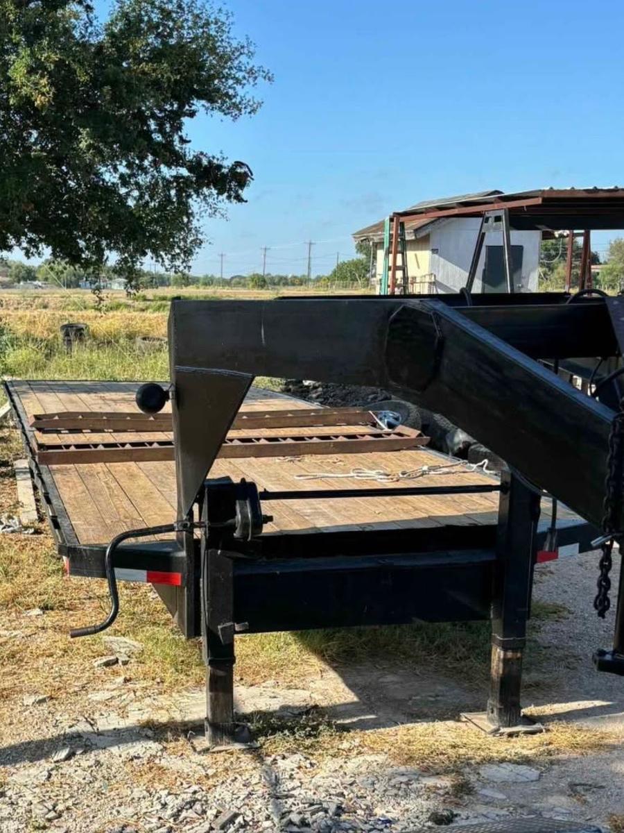 Gooseneck end of a black flatbed trailer with a wood deck and drop-down jack legs