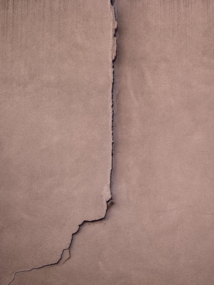 Vertical crack running down a stucco wall against a blue sky