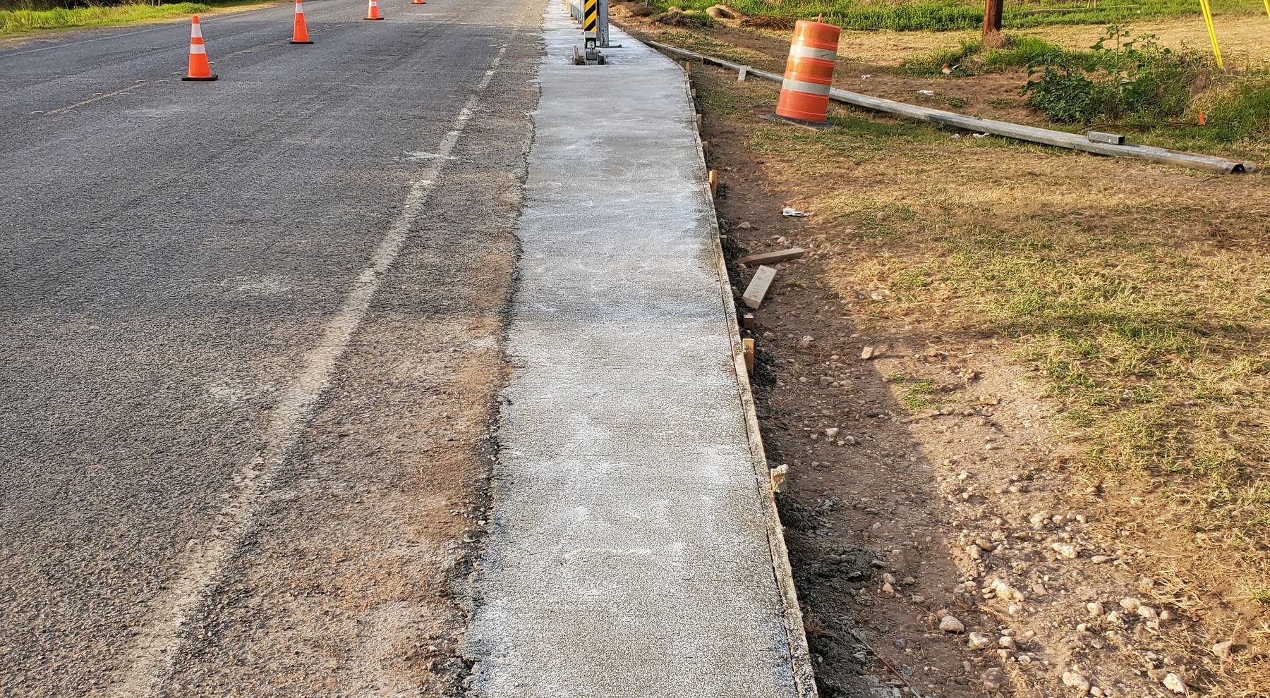 Fresh concrete placed along a roadway beside traffic cones