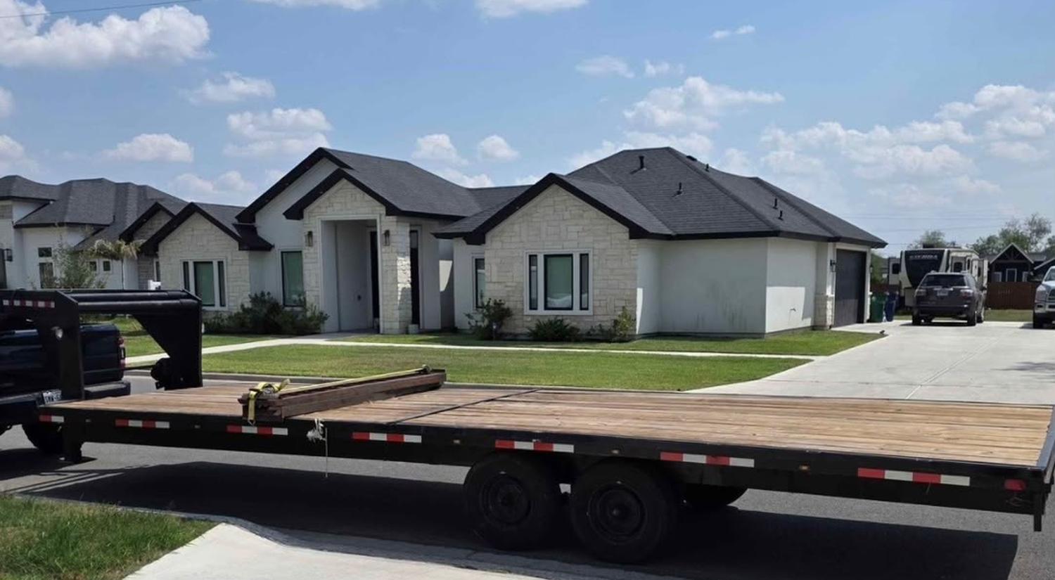 Black gooseneck flatbed trailer with a wood deck parked on a residential street in South Texas