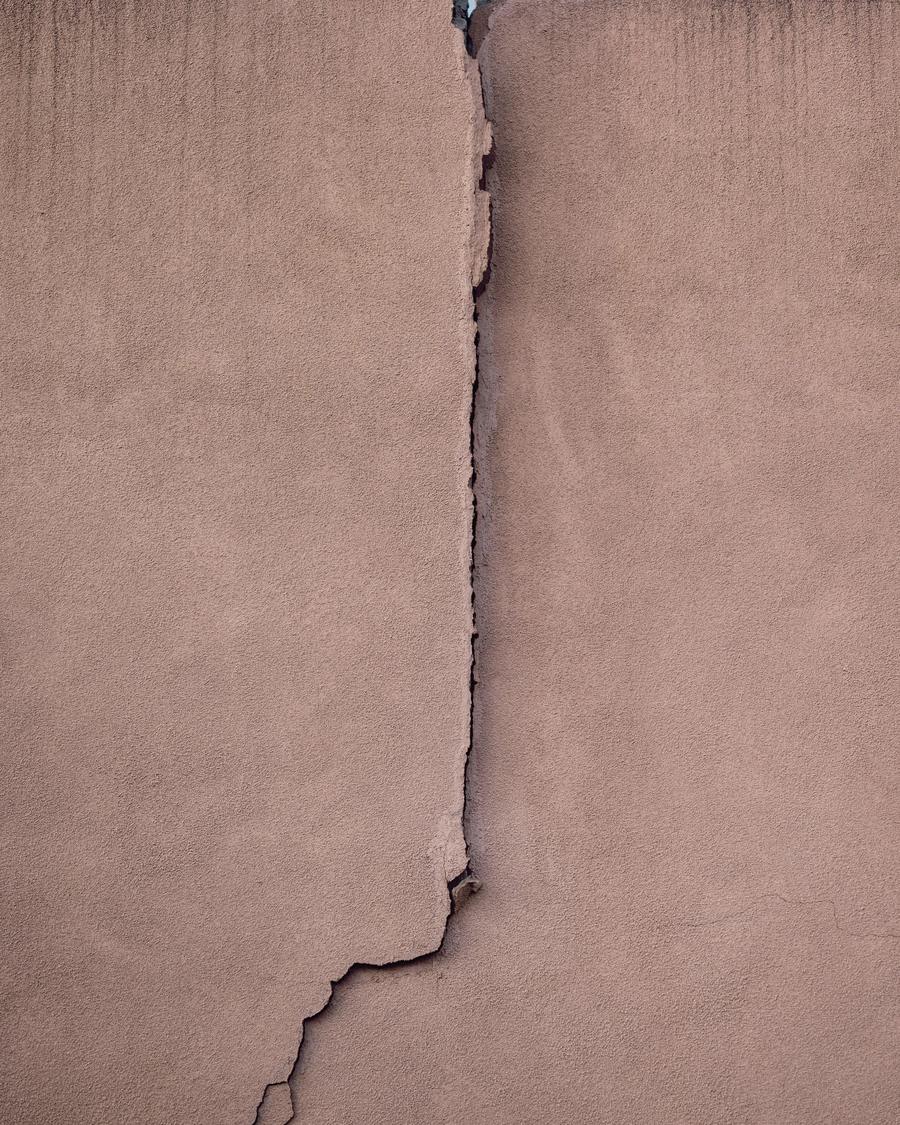Vertical crack running down a stucco wall against a blue sky