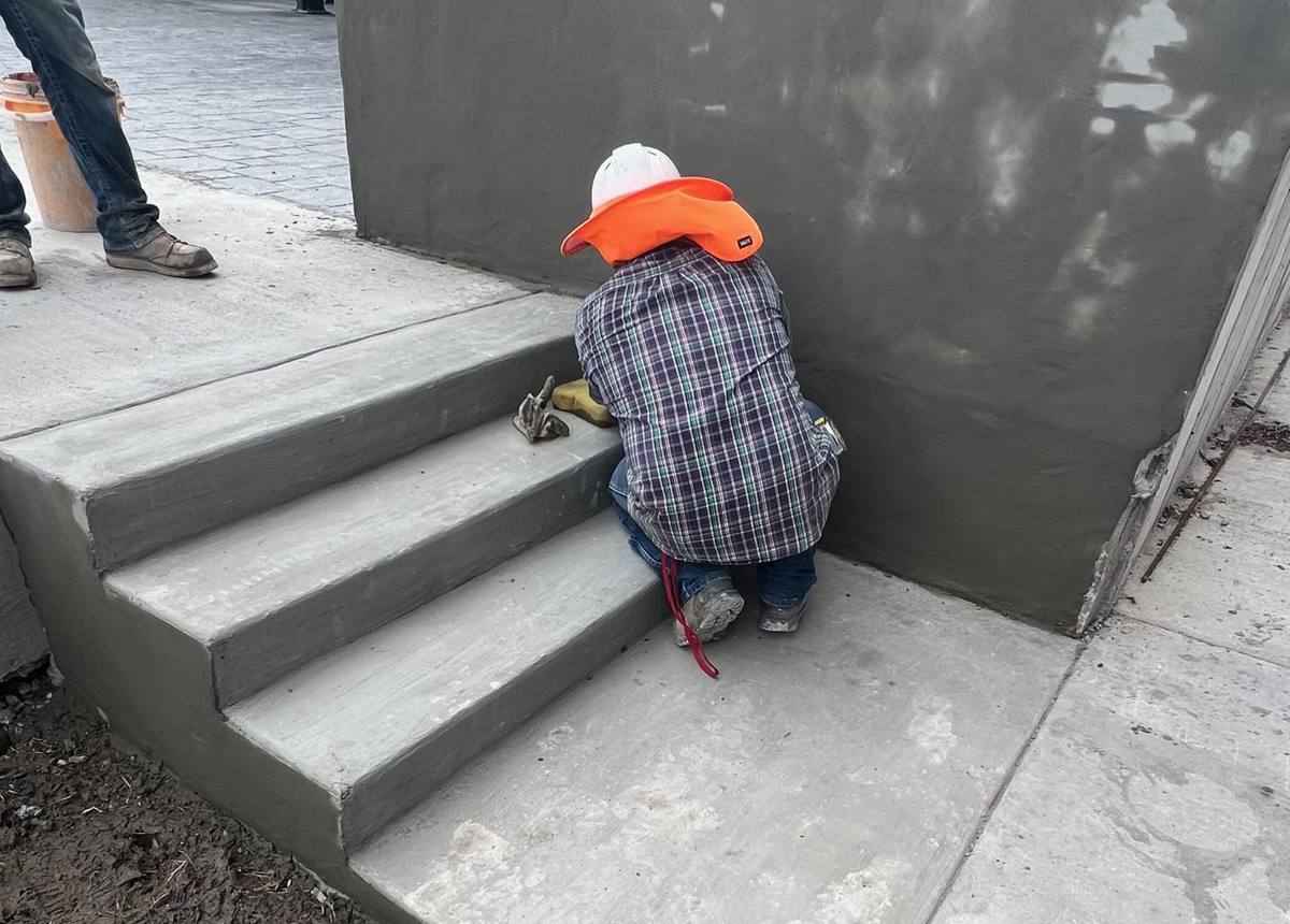 Worker finishing concrete steps beside a retaining wall