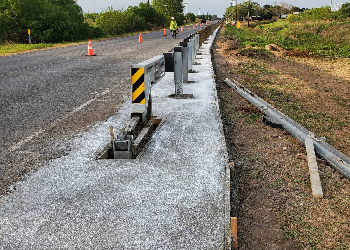 Fresh concrete shoulder beside a roadside guardrail